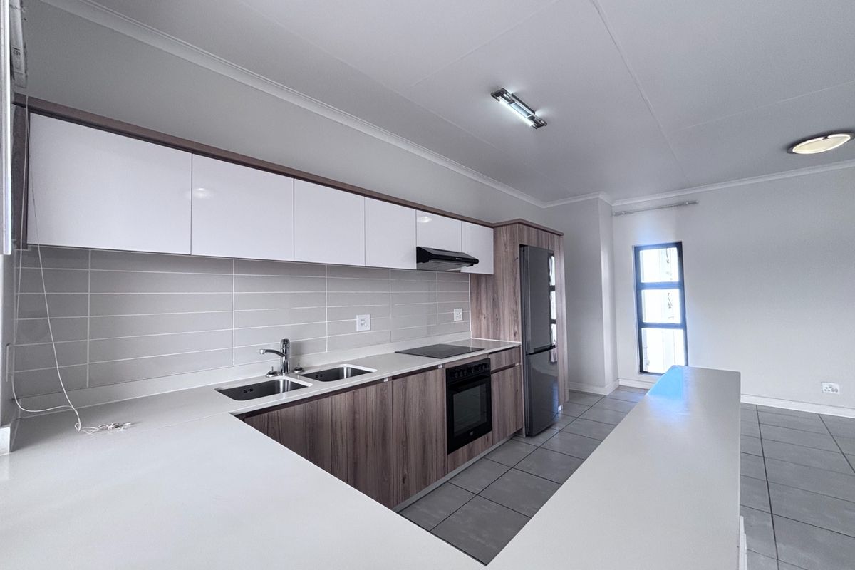 Modern kitchen featuring sleek white and wood-grain cabinetry, stone countertops, integrated appliances, and a functional breakfast bar layout.
