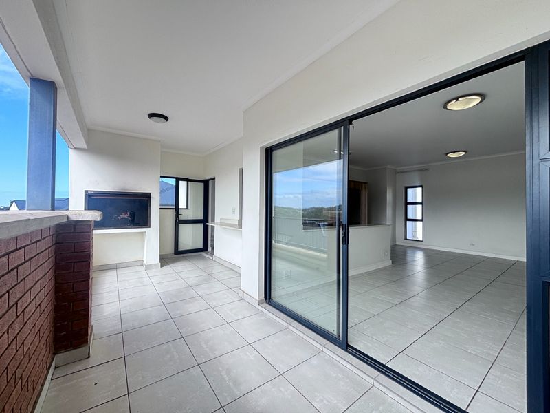Spacious covered balcony featuring tiled flooring, a built-in braai, and large sliding glass doors providing seamless access to the interior living area.
