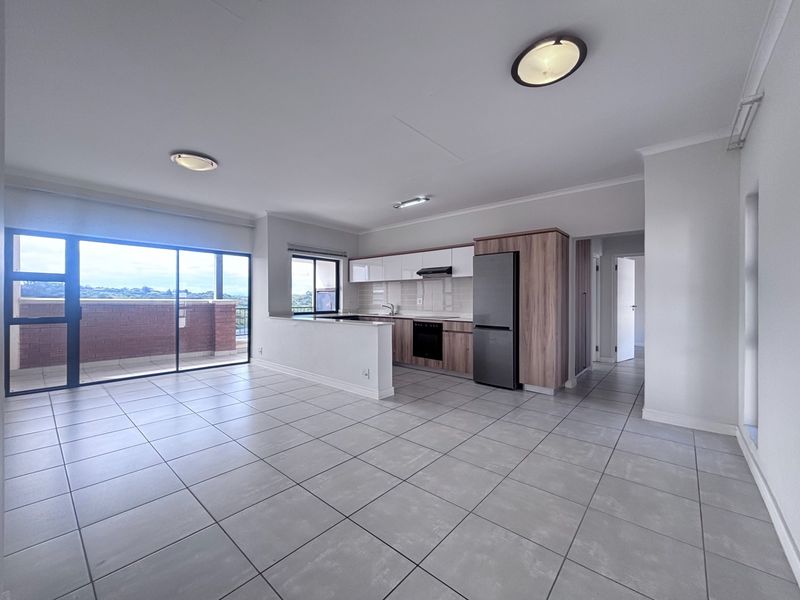 Spacious open-plan living and kitchen area featuring modern cabinetry, tiled floors, and large sliding doors leading to a private balcony with scenic views.