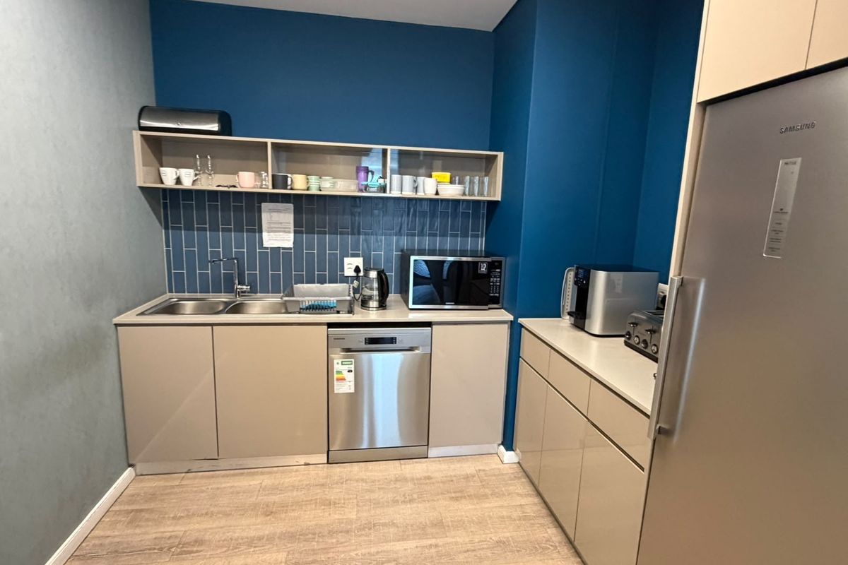 A modern office kitchenette featuring sleek cabinetry, a subway tile backsplash, integrated dishwasher, and built-in microwave, providing a functional and clean break area.