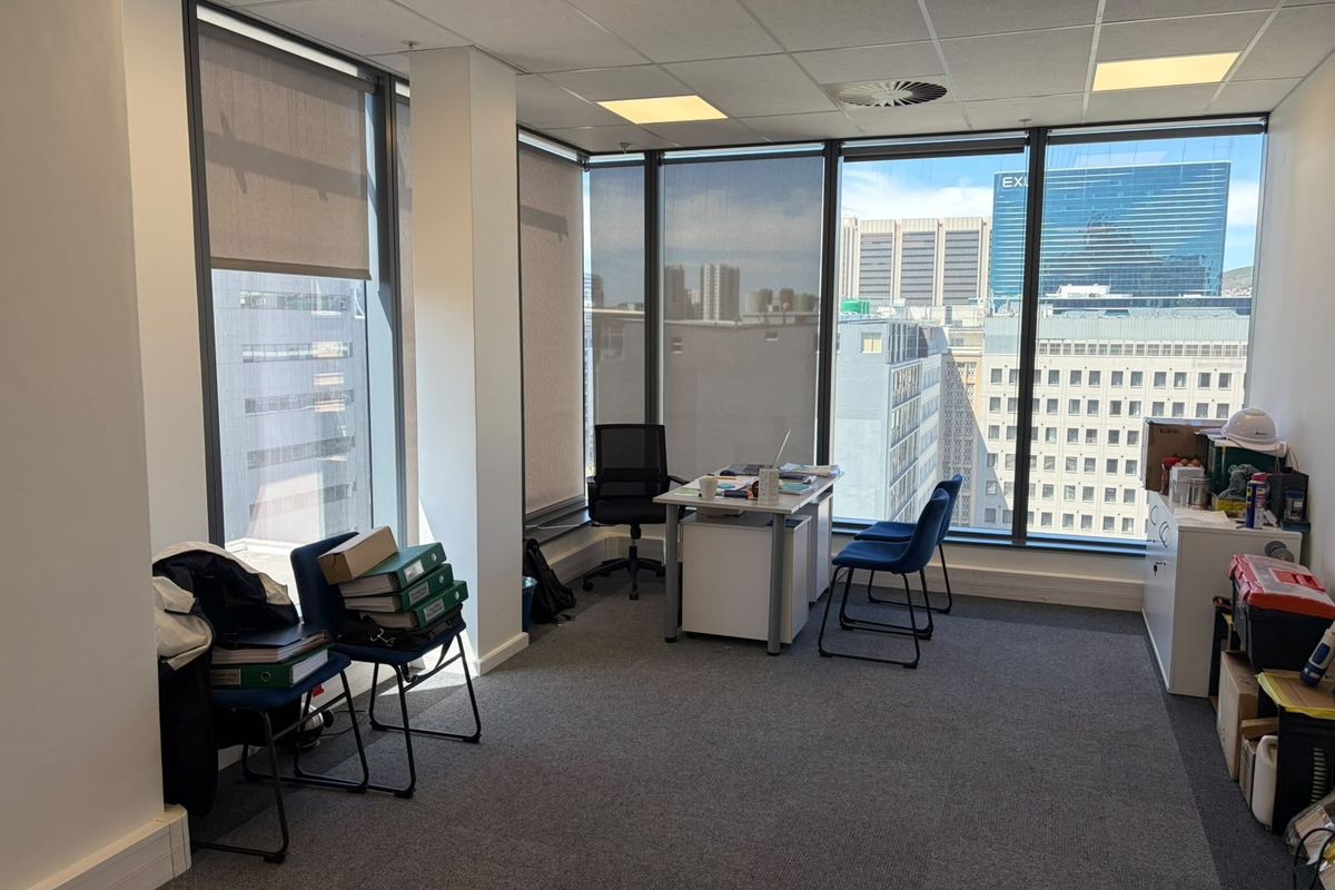 A bright office space featuring floor-to-ceiling windows with city views, carpeted flooring, and a suspended ceiling with integrated lighting.