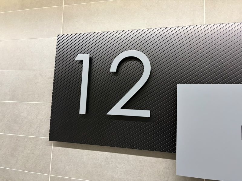 A close-up view of modern office signage featuring the number 12 mounted on a textured black panel against a tiled wall.