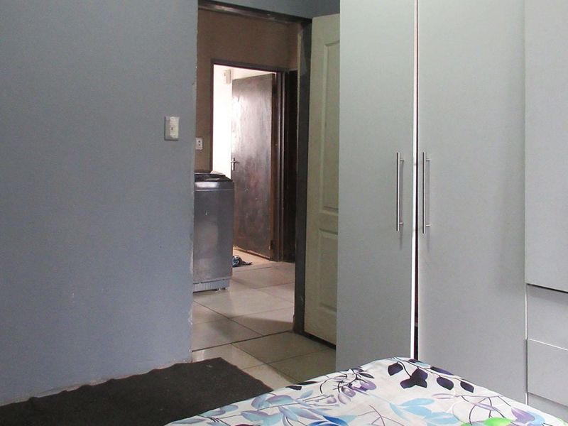 Bedroom featuring built-in cupboards and tiled flooring, with a view through to an adjacent utility area.