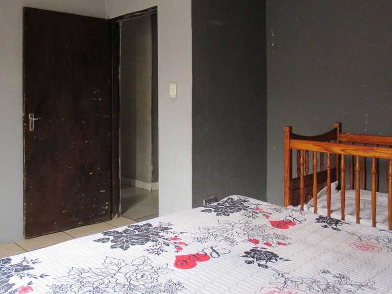 A bedroom featuring tiled flooring and a dark internal door, with walls showing signs of wear and scuffing.