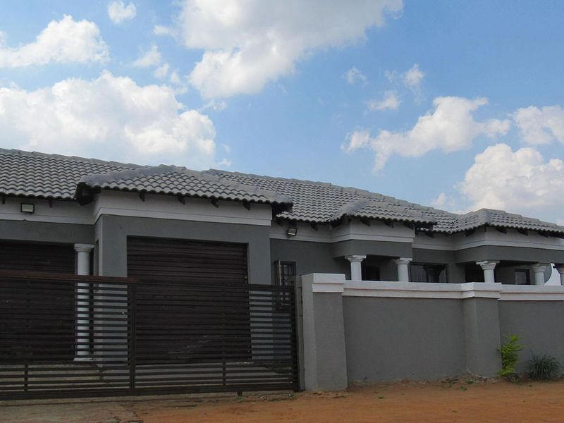 Front elevation of a modern house featuring a tiled roof, grey exterior walls, decorative columns, and a secure perimeter wall with a sliding gate.