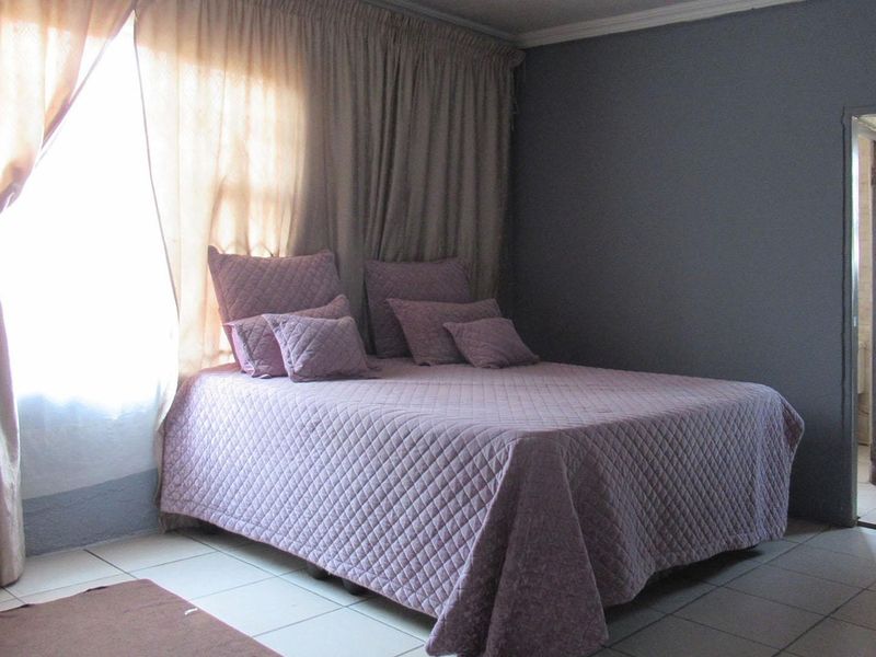 A bedroom featuring tiled flooring and direct access to an en-suite bathroom, requiring minor cosmetic updates to the wall finishes.