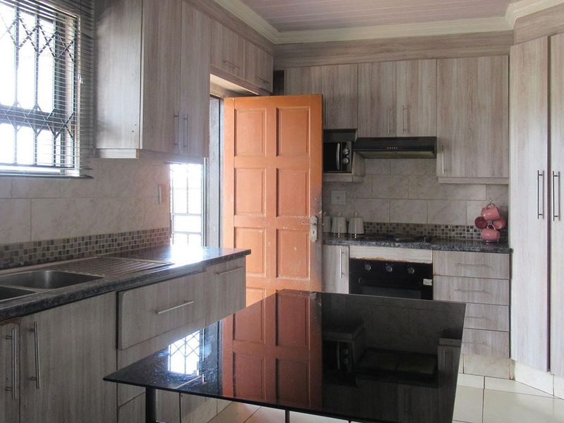 A functional kitchen featuring wood-look cabinetry, granite countertops, a double sink, and built-in cooking appliances with a tiled backsplash.
