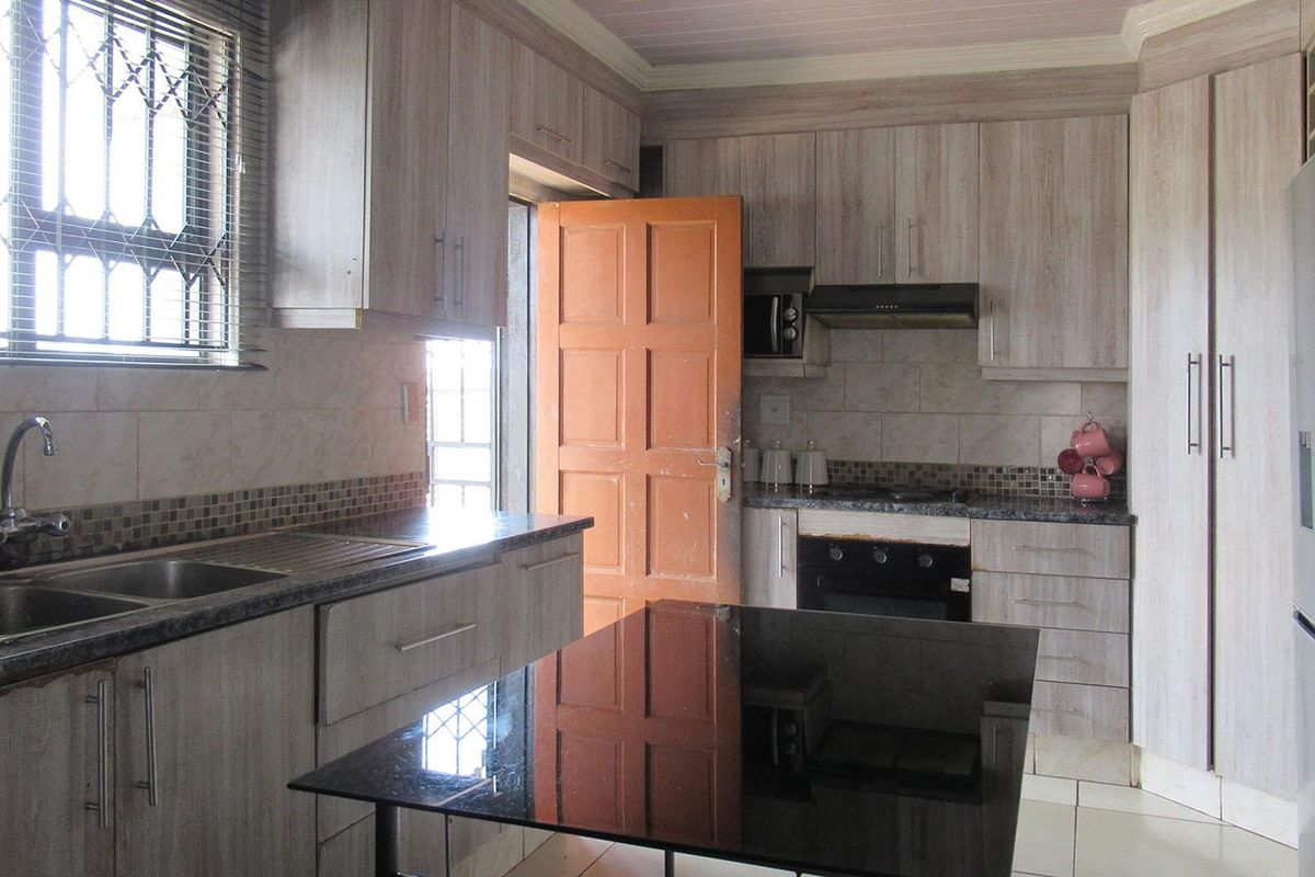A functional kitchen featuring wood-look cabinetry, granite countertops, a double sink, and built-in cooking appliances with a tiled backsplash.