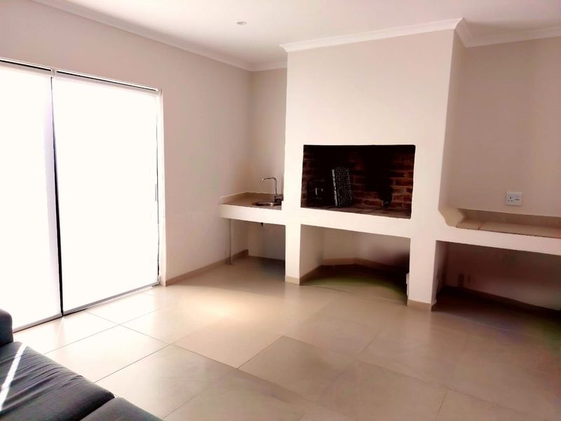 An indoor entertainment area featuring a built-in braai, prep sink, masonry counter, and large sliding glass doors leading to the exterior.