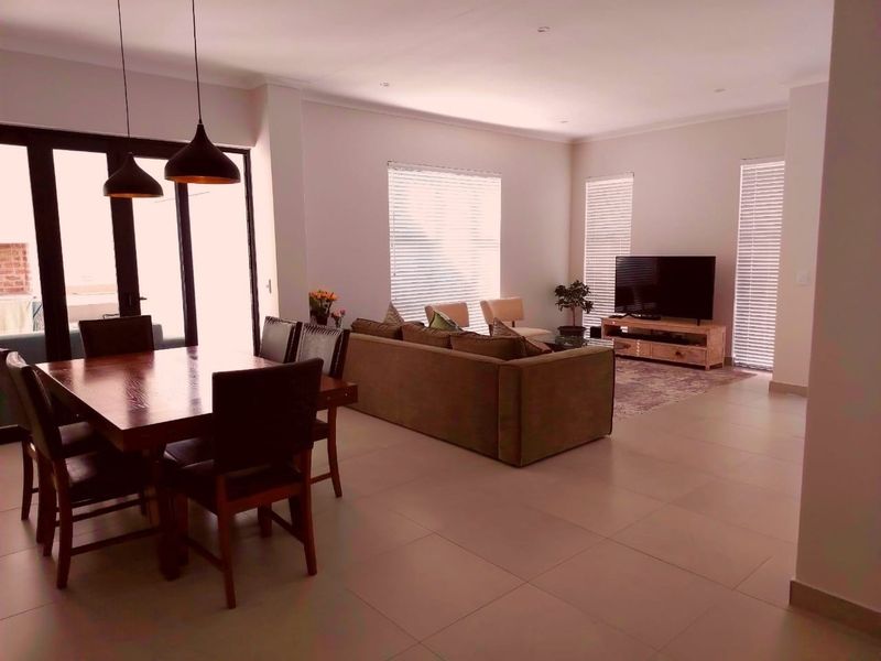 Spacious open-plan living and dining area featuring neutral tiled flooring, modern recessed lighting, and large sliding glass doors leading to the outdoor space.