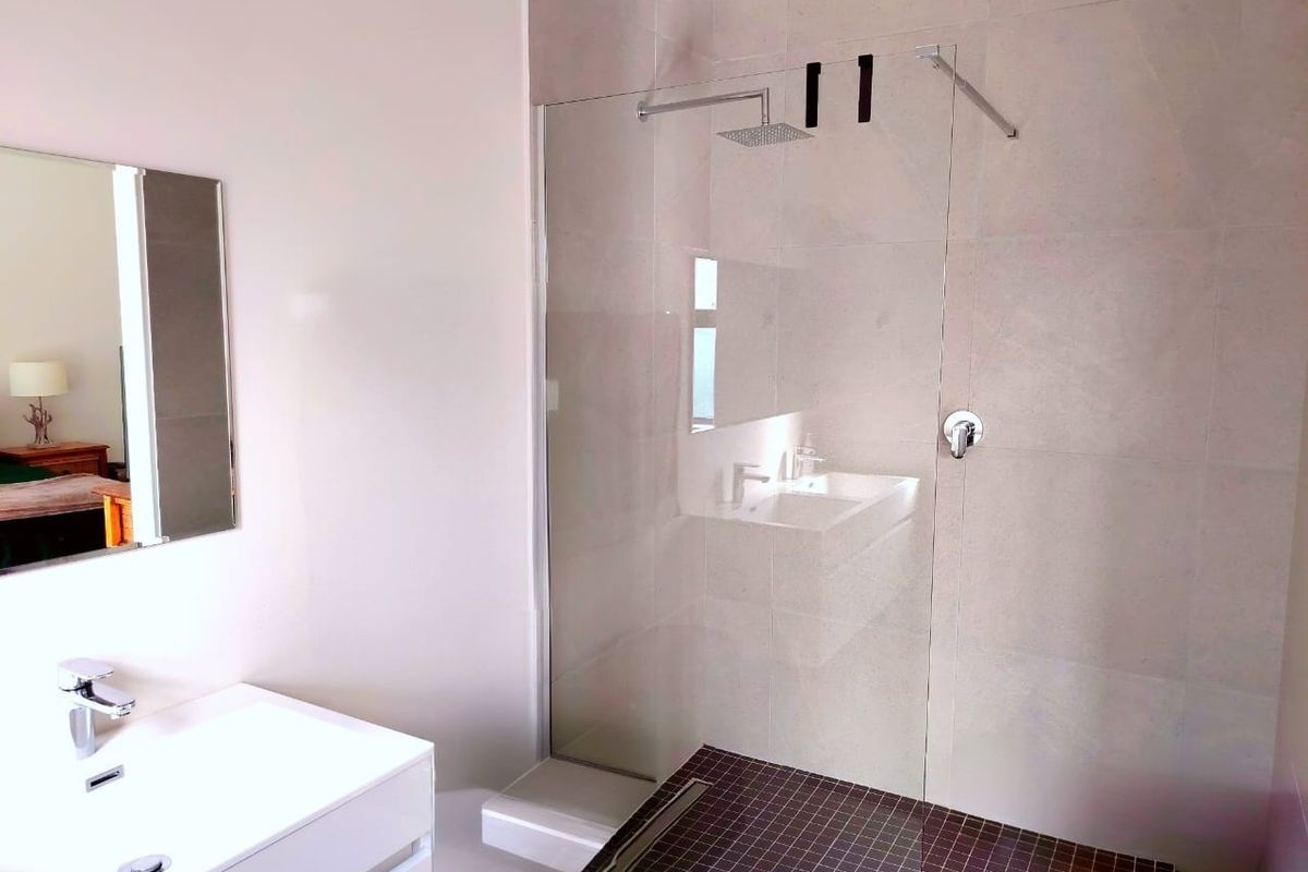 Modern bathroom featuring a spacious walk-in shower with a glass screen, rain shower head, and a sleek wall-mounted vanity with a basin.