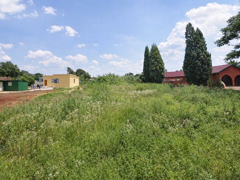 A large, undeveloped residential plot featuring overgrown vegetation, situated in a neighborhood with existing structures and perimeter walling.
