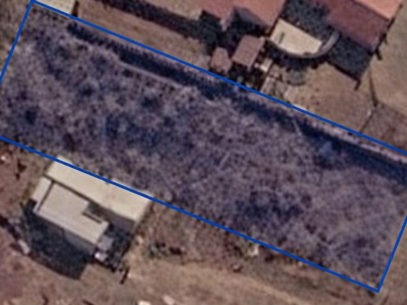 Aerial view of a vacant residential plot outlined in blue, showing the land boundaries and surrounding area.