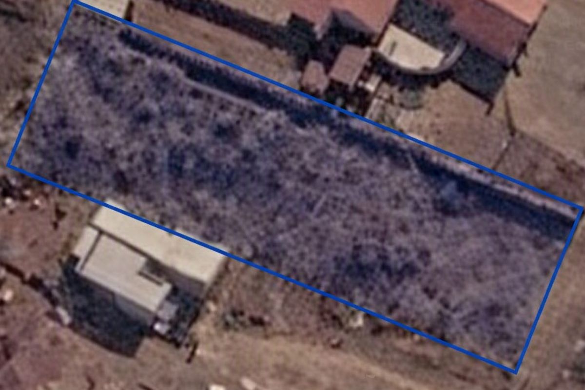 Aerial view of a vacant residential plot outlined in blue, showing the land boundaries and surrounding area.