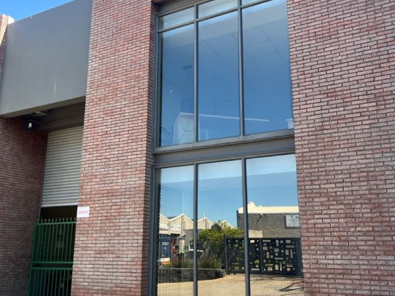 Modern office building exterior featuring a striking red brick facade, large double-height glass windows, and a secure roller shutter entrance.
