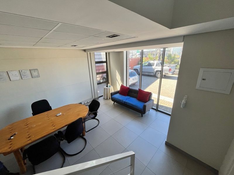 A bright office space featuring tiled flooring, a suspended ceiling with recessed lighting, and large floor-to-ceiling windows providing natural light and exterior access.