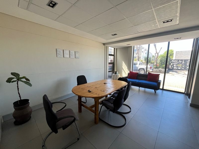A bright office space featuring large glass windows, tiled flooring, and a suspended ceiling with recessed lighting.