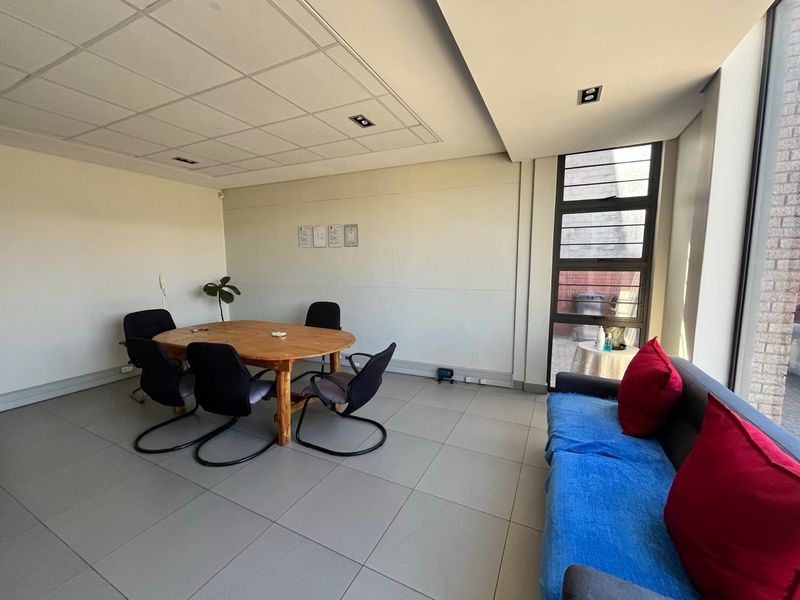 A functional office space featuring tiled flooring, a suspended ceiling with recessed lighting, and a large window providing natural light.