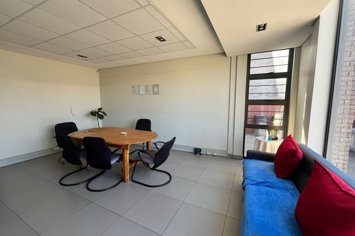 A functional office space featuring tiled flooring, a suspended ceiling with recessed lighting, and a large window providing natural light.