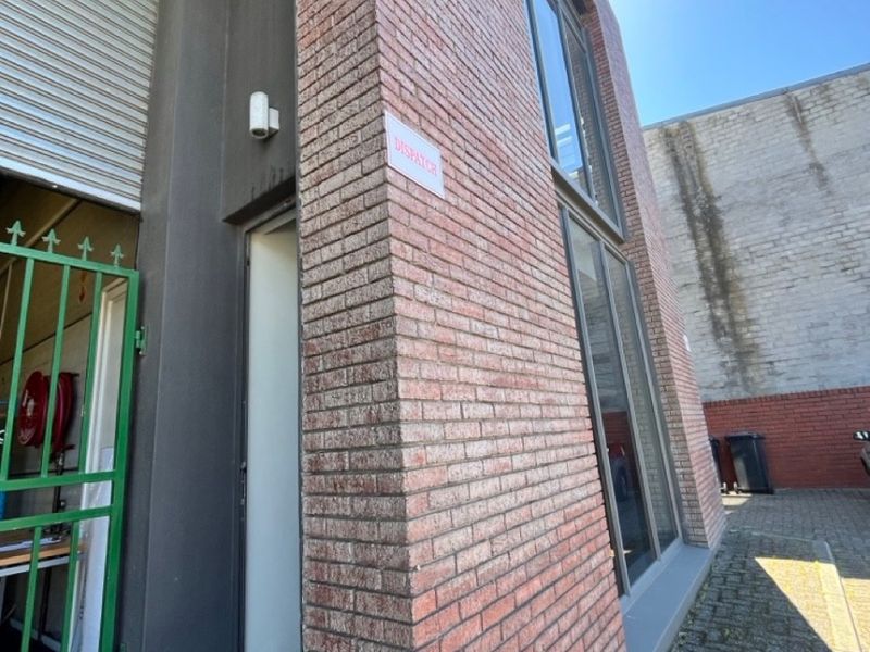 Exterior view of the office building featuring an exposed brick facade, roller shutter door, and paved rear courtyard area.