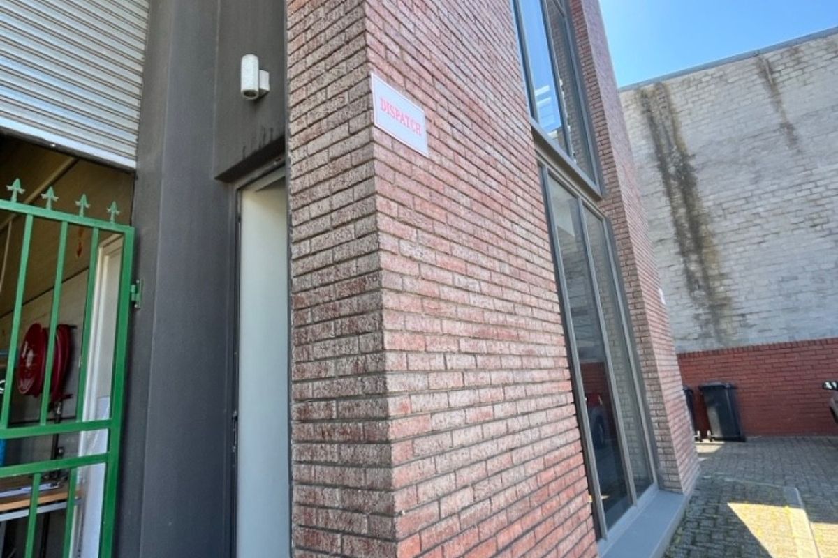 Exterior view of the office building featuring an exposed brick facade, roller shutter door, and paved rear courtyard area.