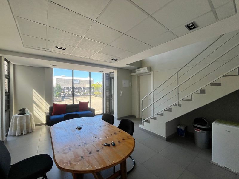 A bright, open-plan office space featuring tiled flooring, a modern staircase, recessed ceiling lighting, and large windows providing ample natural light.