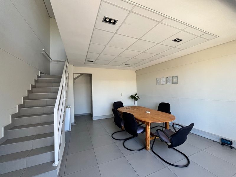 A functional office space featuring tiled flooring, a suspended ceiling with recessed lighting, and an integrated staircase leading to an upper level.