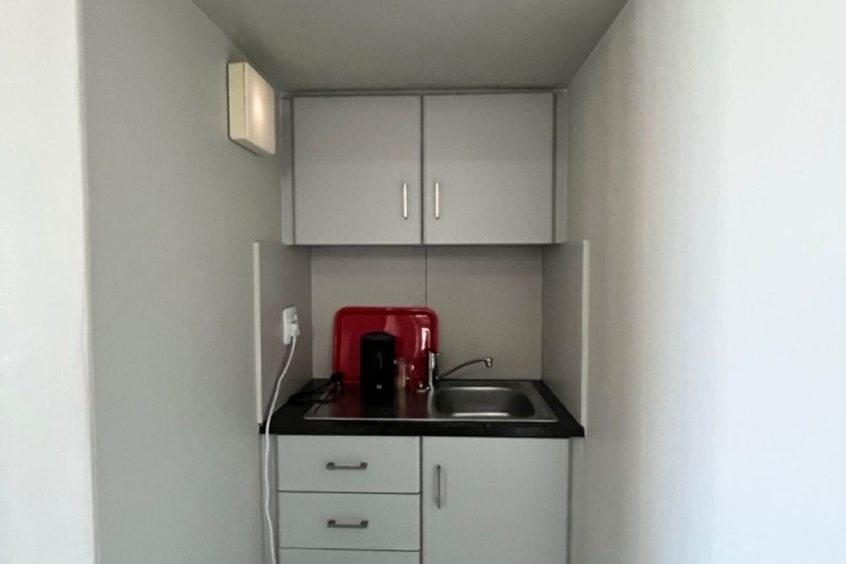 A compact kitchenette featuring built-in cabinetry, a stainless steel sink, and a laminate countertop, providing essential utility in a small office space.