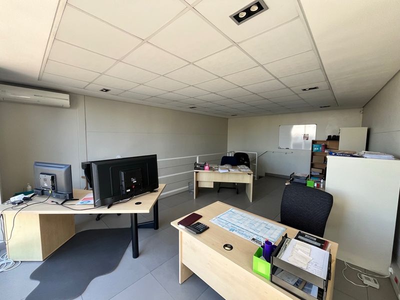 A functional office space featuring a suspended ceiling with recessed lighting, tiled flooring, and a wall-mounted split-system air conditioner.