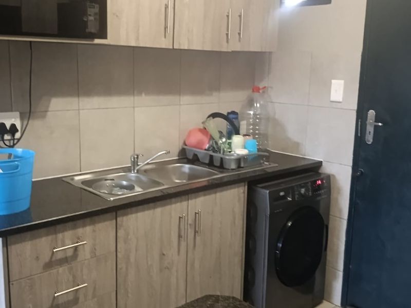 Compact kitchen featuring wood-look cabinetry, laminate countertops, a stainless steel double sink, and a tiled backsplash with integrated microwave space.