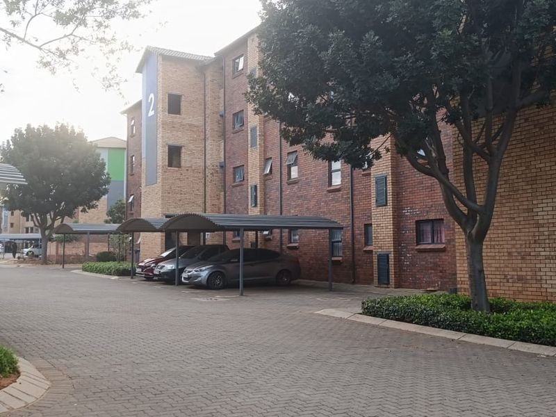 Exterior view of a multi-story apartment complex featuring face brick construction, paved driveway, and covered parking bays.