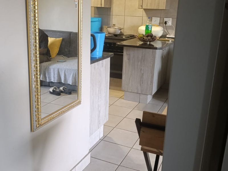 An open-plan kitchen area featuring tiled flooring, granite countertops, and built-in cabinetry, viewed from an adjacent hallway.