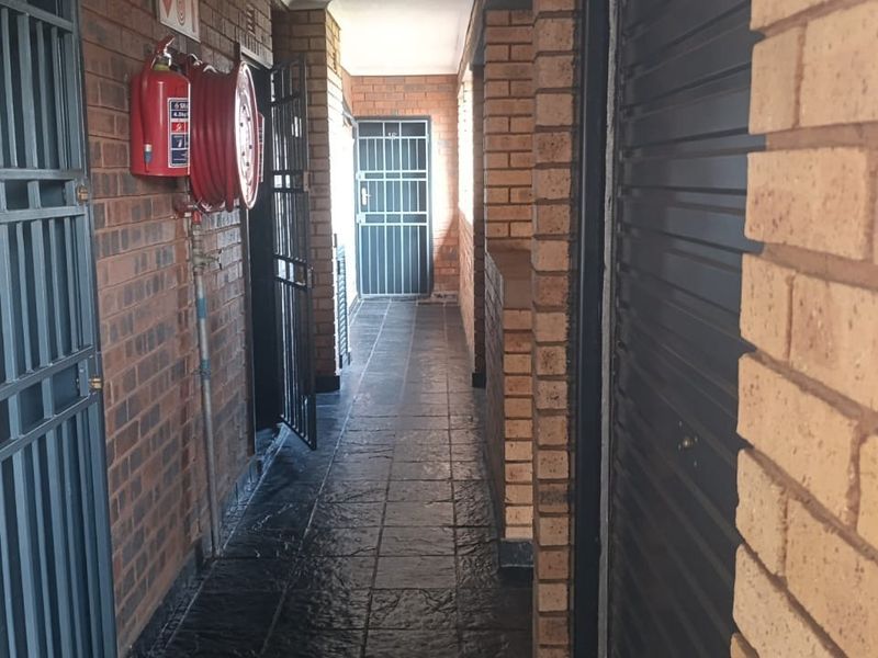 A functional apartment hallway featuring exposed brick walls, tiled flooring, and integrated security gates with essential fire safety equipment installed.