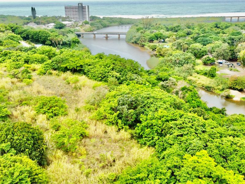 Aerial view of a vacant residential plot featuring lush vegetation, river frontage, and proximity to the coastline and local infrastructure.