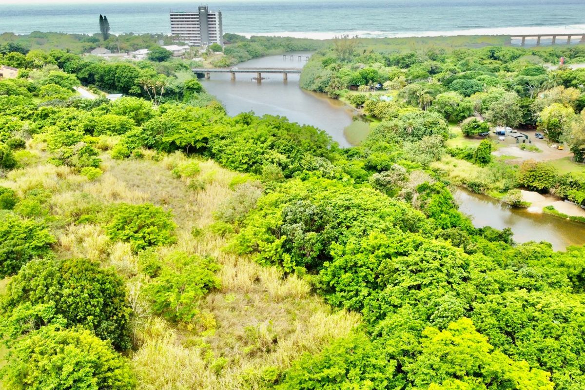 Aerial view of a vacant residential plot featuring lush vegetation, river frontage, and proximity to the coastline and local infrastructure.