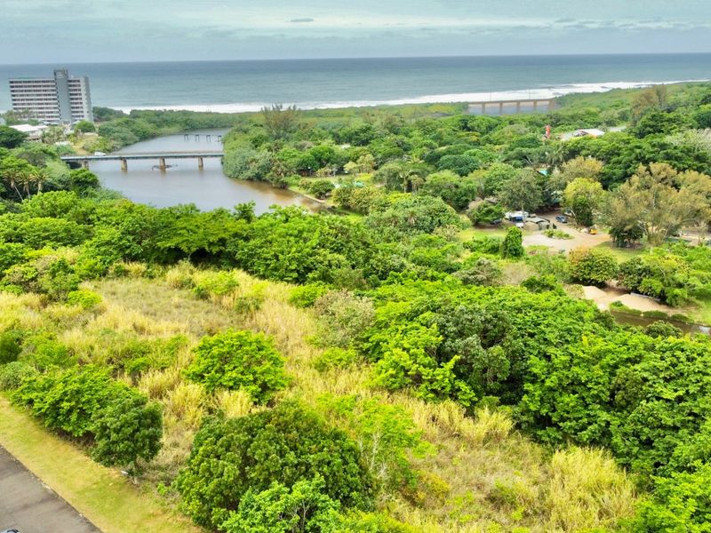 Aerial view of a vacant residential plot featuring lush coastal vegetation, river frontage, and proximity to the ocean and local infrastructure.