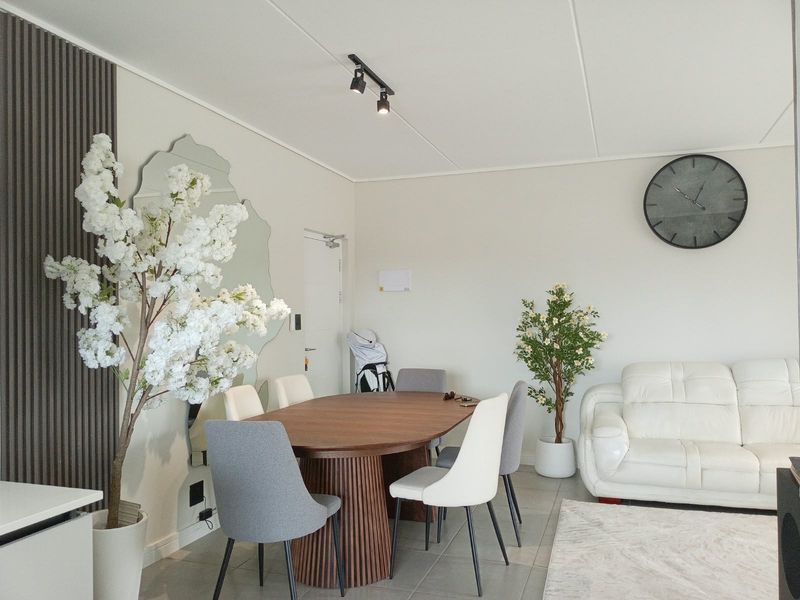 A bright open-plan living and dining area featuring modern track lighting, decorative slatted wall paneling, and neutral tiled flooring.