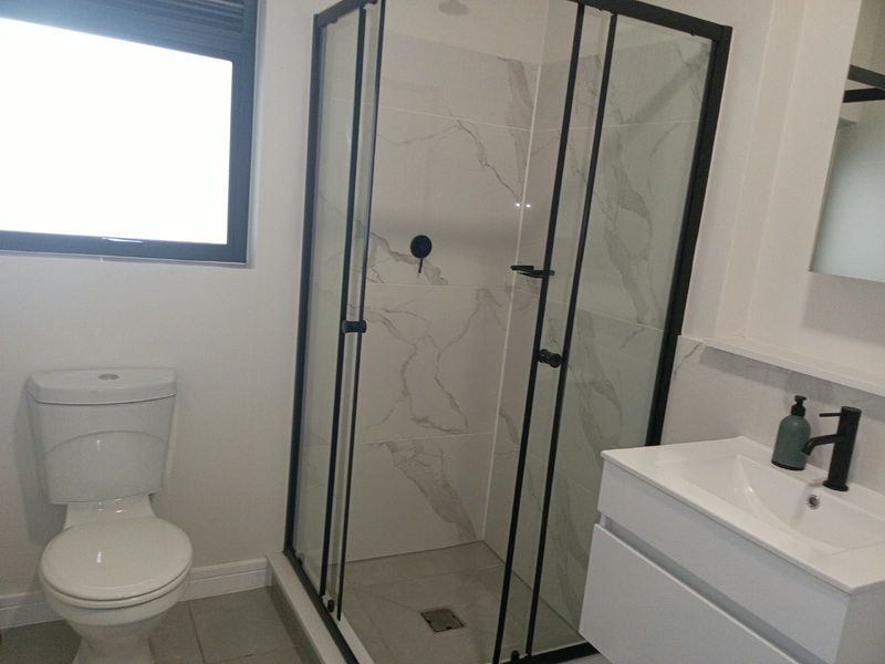 Modern bathroom featuring a walk-in shower with black frame, marble-look wall tiles, a contemporary vanity unit, and a standard toilet.