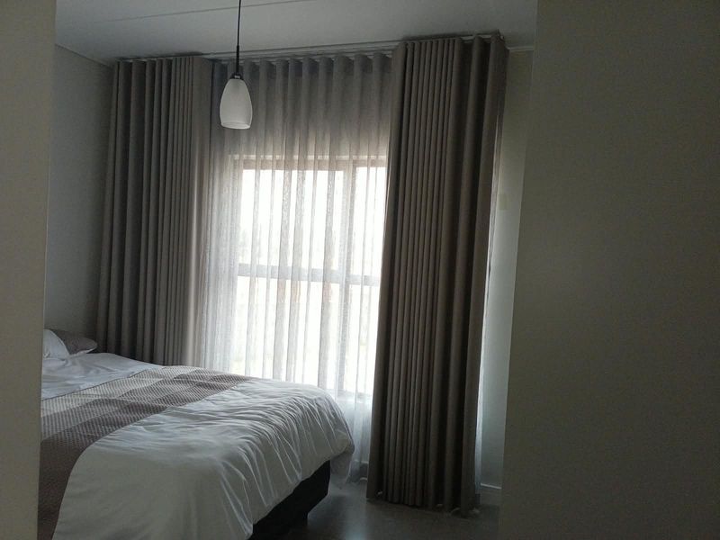 A well-lit bedroom featuring floor-to-ceiling curtains and a modern pendant light fixture.
