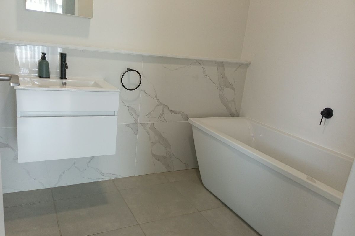 Modern bathroom featuring a sleek wall-mounted vanity, a contemporary freestanding bathtub, and elegant marble-look wall tiling with matte black fixtures.