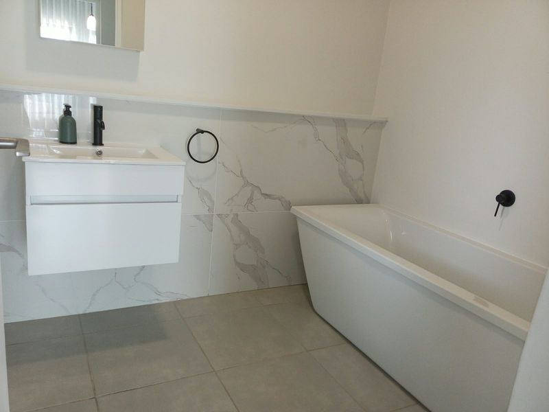 Modern bathroom featuring a sleek wall-mounted vanity, a contemporary freestanding bathtub, and elegant marble-look wall tiling with matte black fixtures.