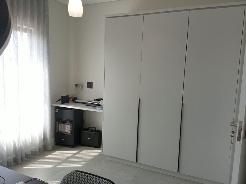 A bedroom featuring a large built-in wardrobe, a built-in desk area, and neutral tiled flooring with natural light from the window.