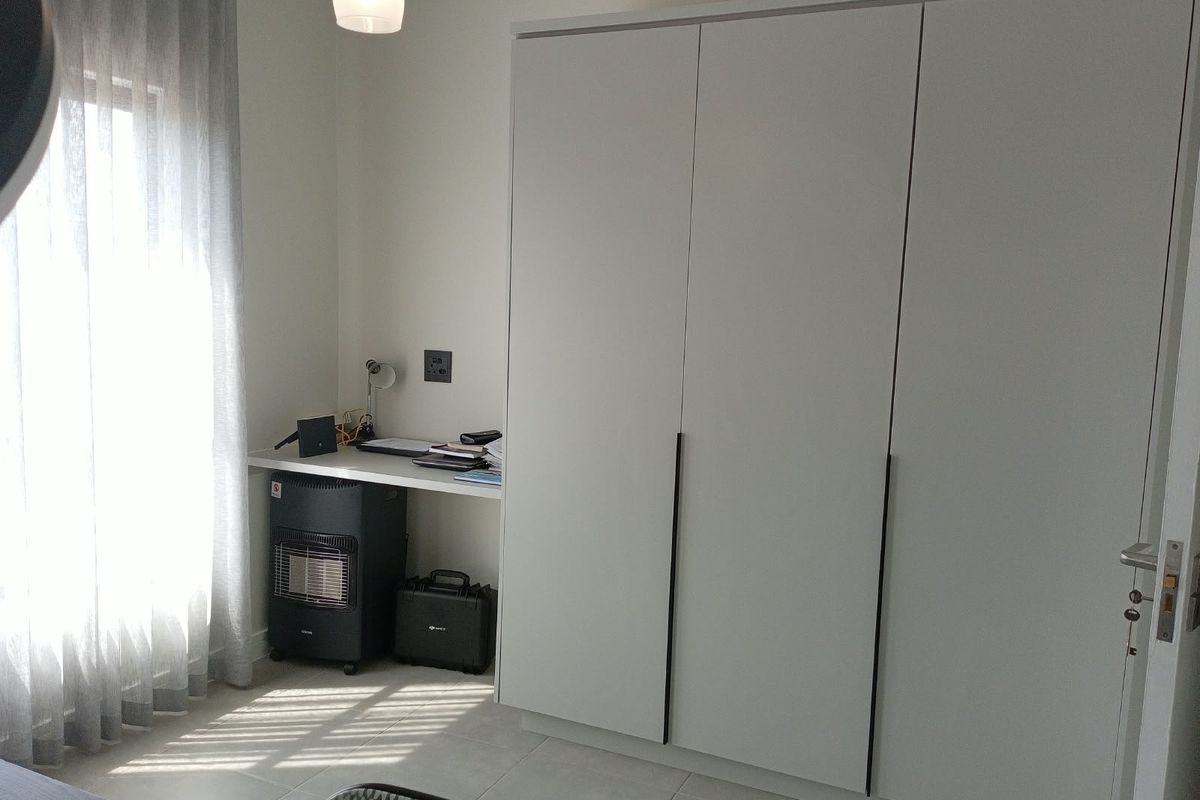 A bedroom featuring a large built-in wardrobe, a built-in desk area, and neutral tiled flooring with natural light from the window.
