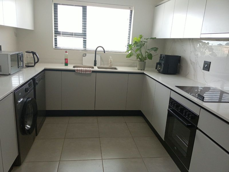 Modern kitchen featuring sleek white cabinetry, stone countertops, marble-look splashback, integrated oven and hob, and tiled flooring.