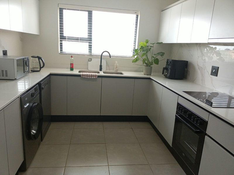 Modern U-shaped kitchen featuring sleek white cabinetry, stone countertops, marble-look splashback, integrated oven, and hob, providing a clean and functional culinary space.