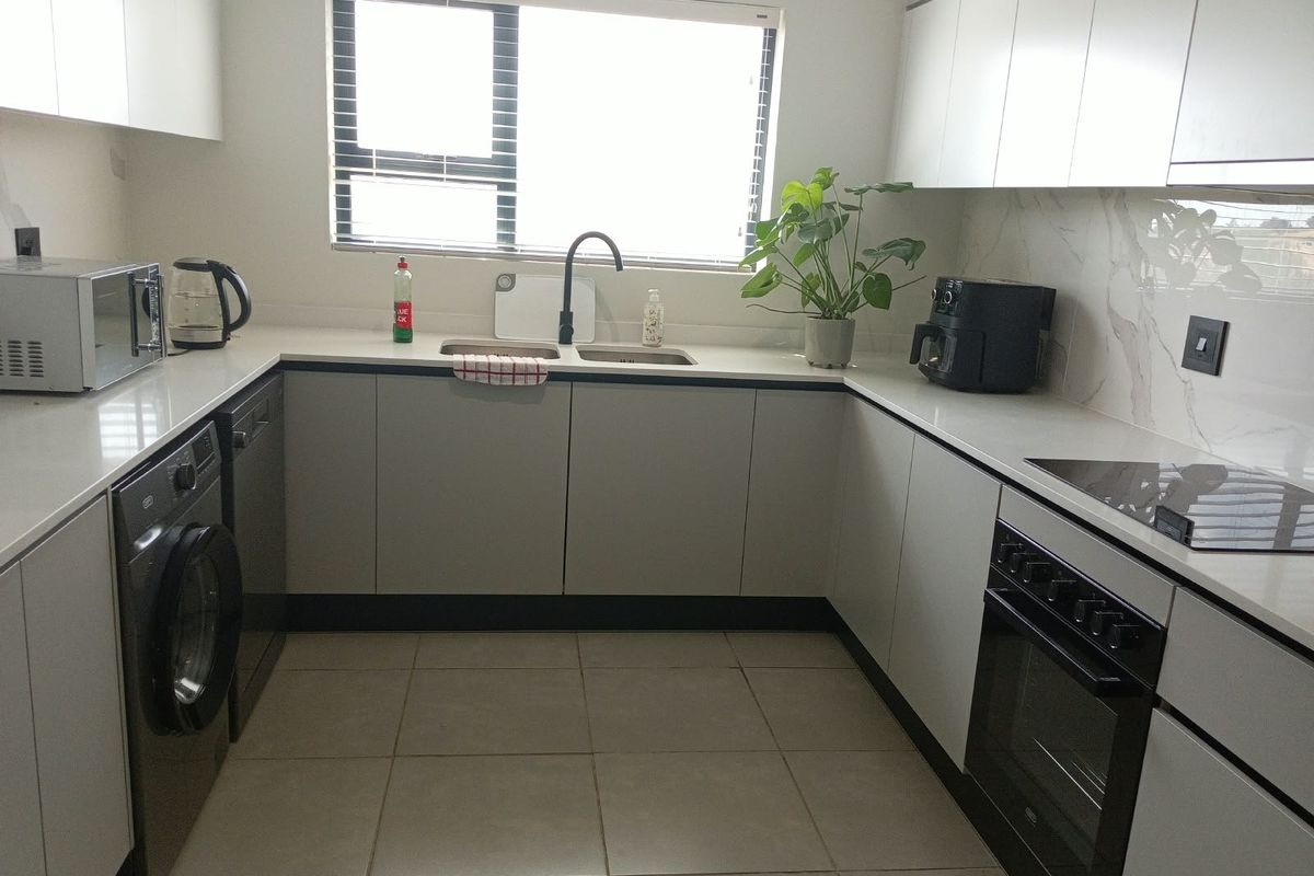 Modern U-shaped kitchen featuring sleek white cabinetry, stone countertops, marble-look splashback, integrated oven, and hob, providing a clean and functional culinary space.
