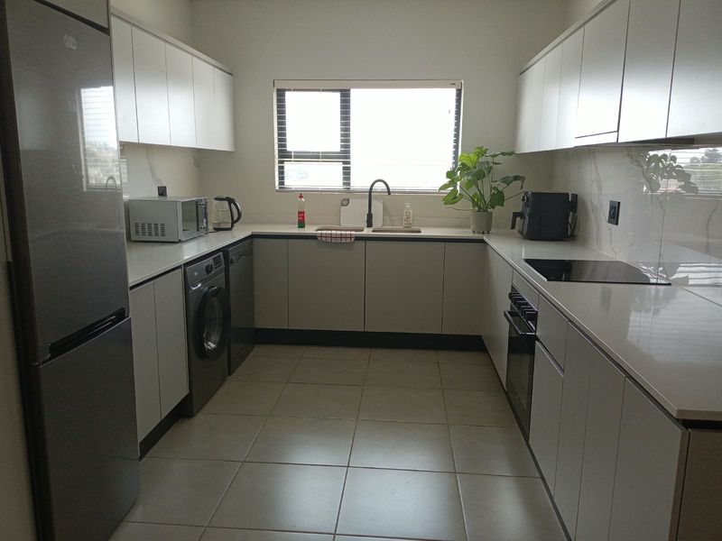 Modern kitchen featuring sleek white cabinetry, stone countertops, integrated appliances, and tiled flooring, offering a clean and functional workspace.