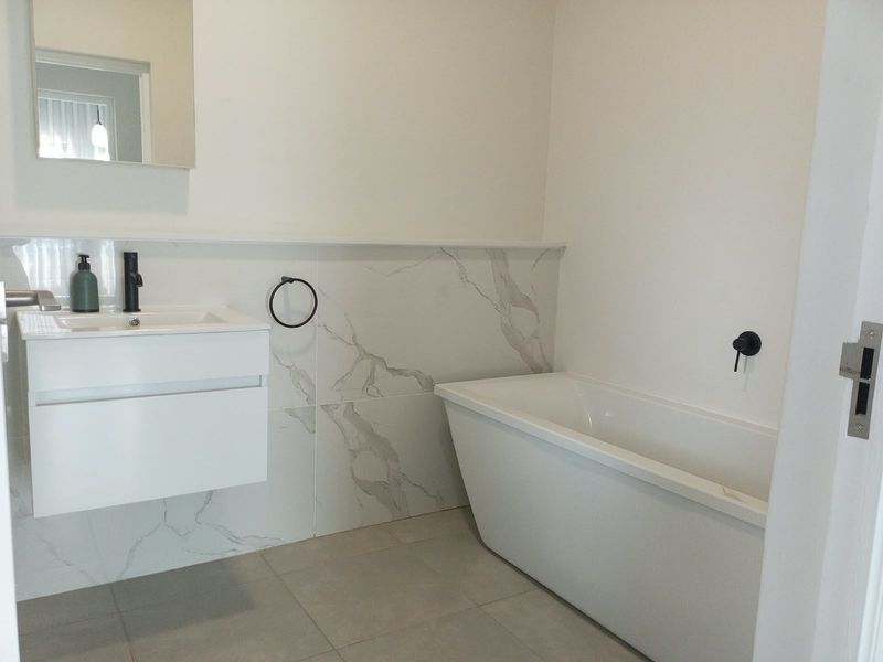 Modern bathroom featuring a sleek wall-mounted vanity, a contemporary freestanding bathtub, and elegant marble-look wall tiling with matte black fixtures.
