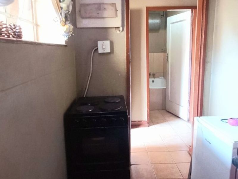 A functional scullery area featuring tiled flooring, an electric stove, and direct access to an adjacent room with a sink.