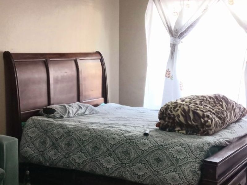 A standard bedroom featuring tiled flooring, a ceiling light, and a window with a curtain rail.